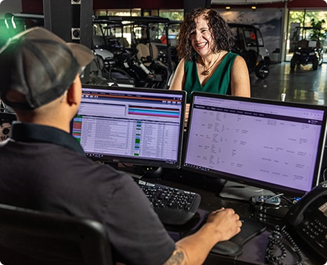 Image of a man behind two computer monitors on a sales floor talking to a customer. Image of a man behind two computer monitors on a sales floor talking to a customer.