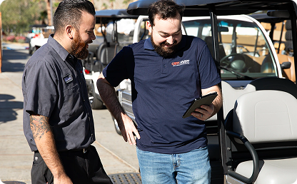 Image of two men looking at a tablet in front of a golf cart. Image of two men looking at a tablet in front of a golf cart.