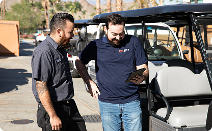 Image of two men looking at a tablet in front of a golf cart. Image of two men looking at a tablet in front of a golf cart.