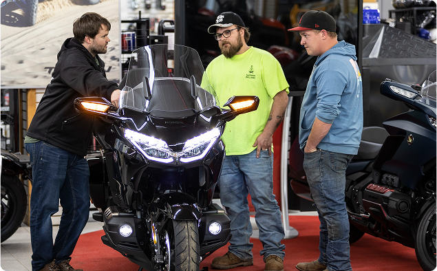 Three men talking to each other on a store floor with motorcycles. Three men talking to each other on a store floor with motorcycles.