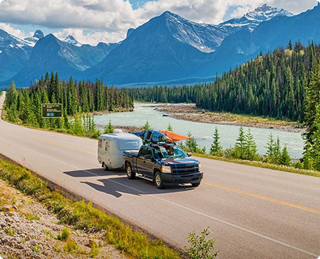 Image of a truck with a trailer driving down a road in front of a lake and a mountain. Image of a truck with a trailer driving down a road in front of a lake and a mountain.